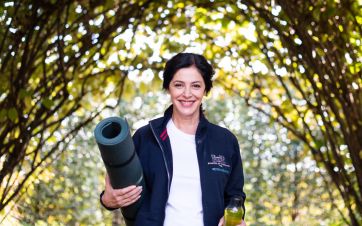 Woman holding a rolled yoga mat, smiling outdoors
