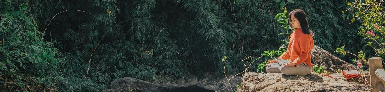 Woman meditating on a rock overlooking a river surrounded by nature during a meditation retreat