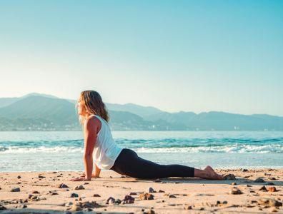 Woman practising yoga in a pose on a sandy beach during a beach yoga retreat