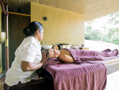 Ayurveda healing Woman lies on a massage bed in a purple towel as an Ayurveda therapist lays hands on her head
