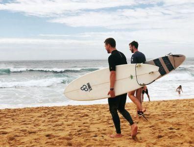 Two men walking towards the sea carrying surf boards during a yoga and surf retreat