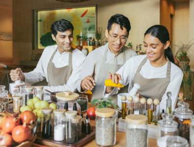 Ayurveda cooking class Man and woman in aprons work with a chef in a cooking class surrounded by fruit and pots of herbs and oils