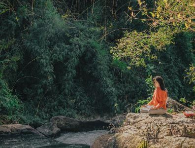 Woman meditating on a rock overlooking a river surrounded by nature during a meditation retreat