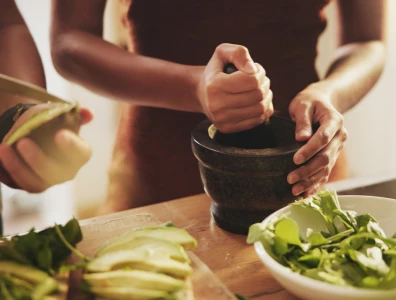 Person grinds herbs surrounded by bowls of greenery
