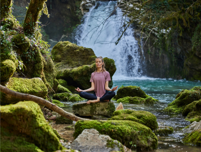 Woman sitting in lotus position on rocks meditating by a waterfall 