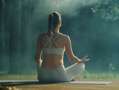 Woman in activewear sits in a meditative pose in a forest setting