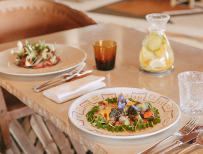 Colourful salads with edible flowers on white plates next to a jug of lemon water