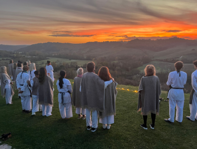Group in loose fitting clothes standing together on a countryside hill watching the sunset