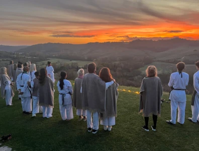 Group in loose fitting clothes standing together on a countryside hill watching the sunset