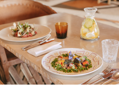 Colourful salads with edible flowers on white plates next to a jug of lemon water