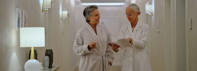 Mature woman in a white robe speaking with a female consultant at a menopause retreat