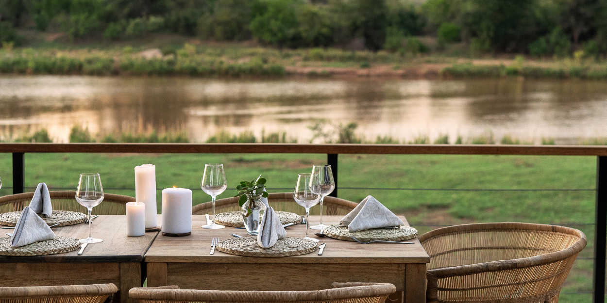 Table laid up with glassware, white napkins and candles with a view of the riverbank