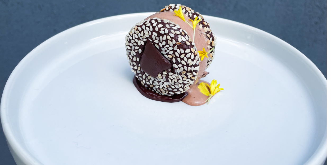 Bitesize dessert on a white plate, with a white seeded covering and edible yellow flowers
