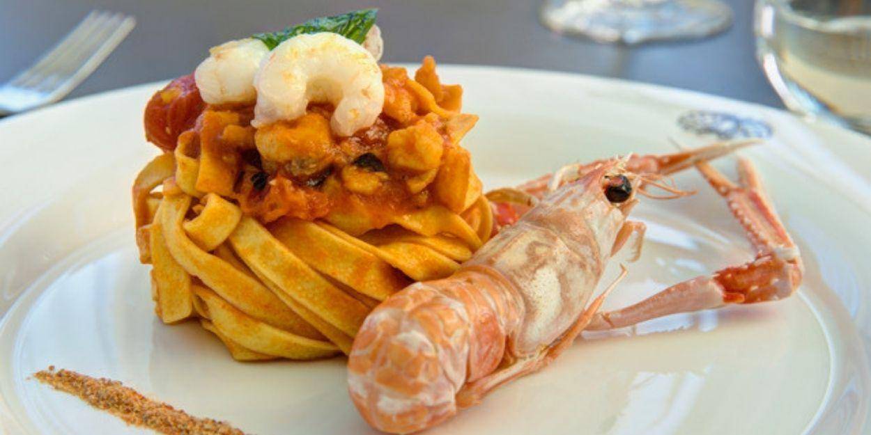 A mound of pasta on a white plate topped with prawns with a prawn that hasn't been shelled to one side