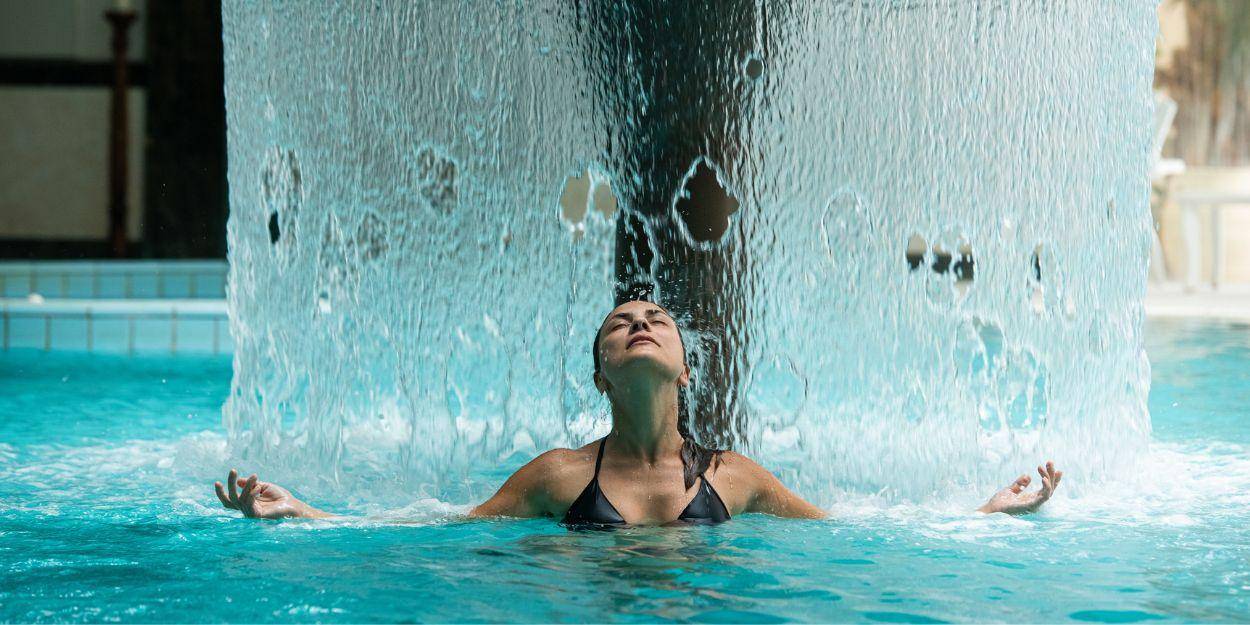 Woman in the thermal pool standing under a fountain of water