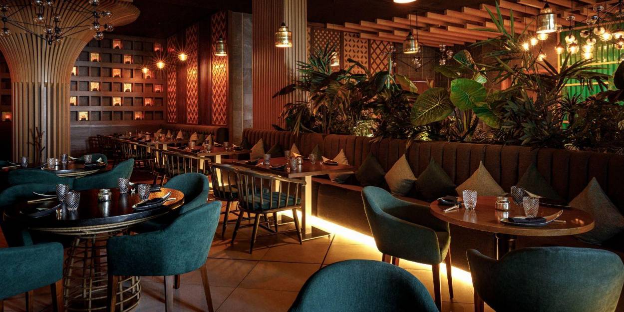 Contemporary dining at Palmaïa – The House of AïA Glamorous restaurant with glossy plants, brown sofa-like seating and blue chairs, dark-wood tables and lantern-like lights