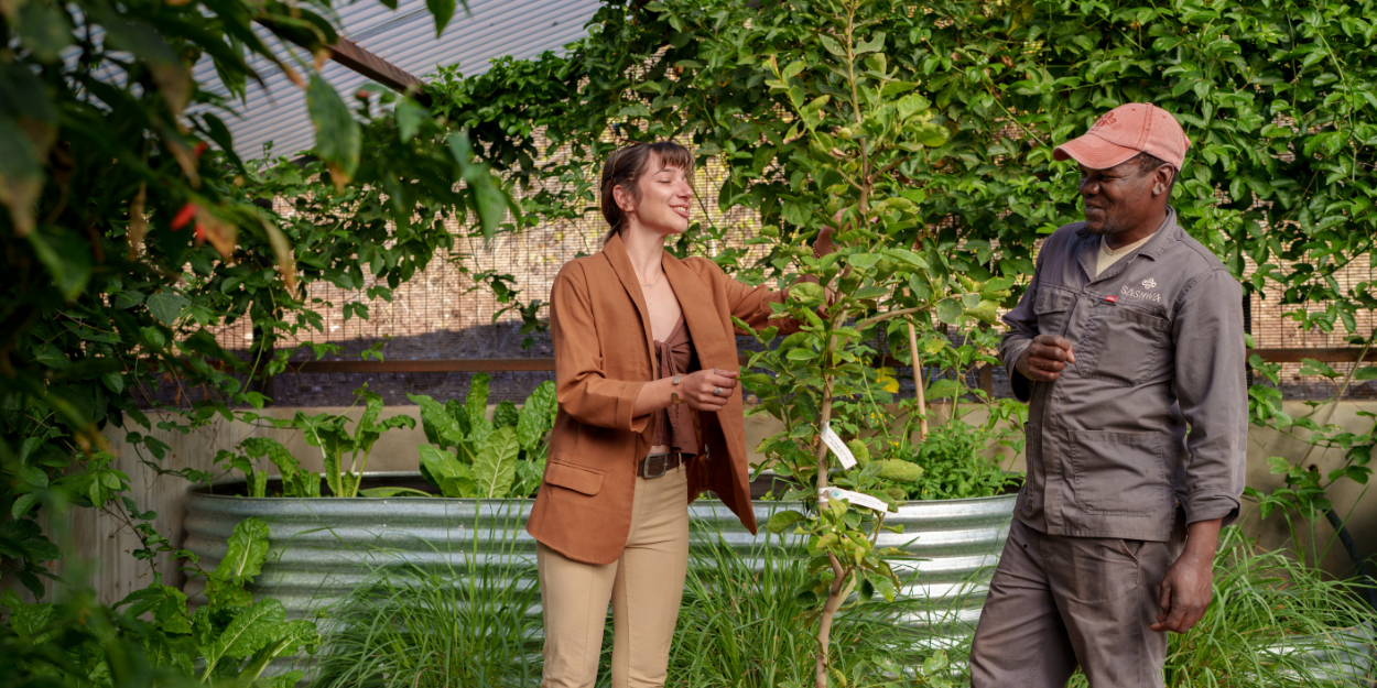 A staff member and female chat in a leafy garden under a blue sky