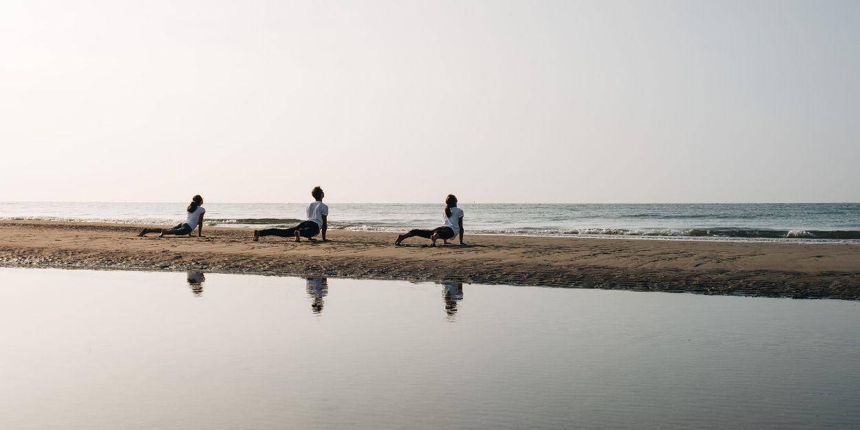 Three people in white practice yoga on the beach under a morning sky