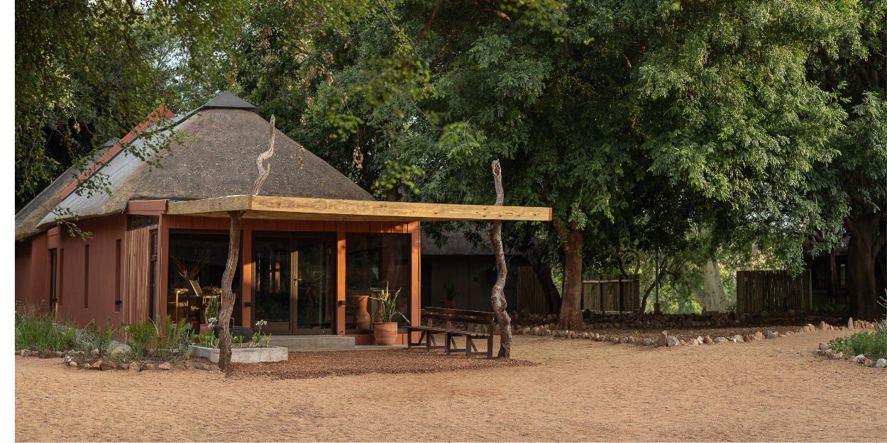 Retreat entrance with a triangular-shaped roof, wooden walls and stilts and soft lighting among thick greenery