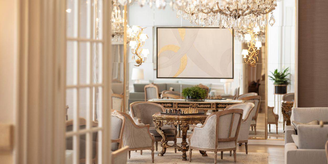 Elegant lounge area with wooden floors, chandeliers, gilded mirrors, patterned rugs and grand armchairs