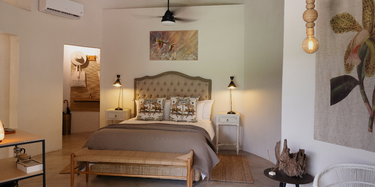 Stylish hotel room with floral wall art, white bedding and a cushioned headboard, a wooden floor, ceiling fan and white walls