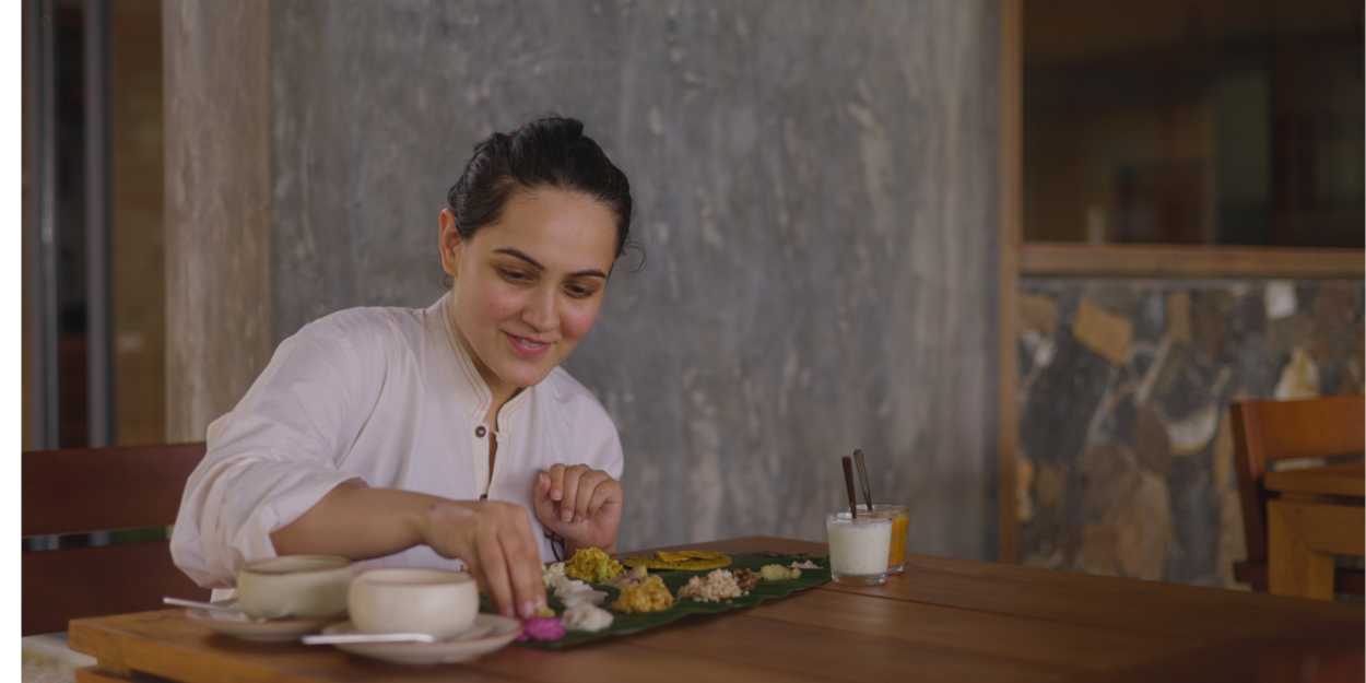 Woman in white sits at a wooden dining table over a plate of food made up of small bites