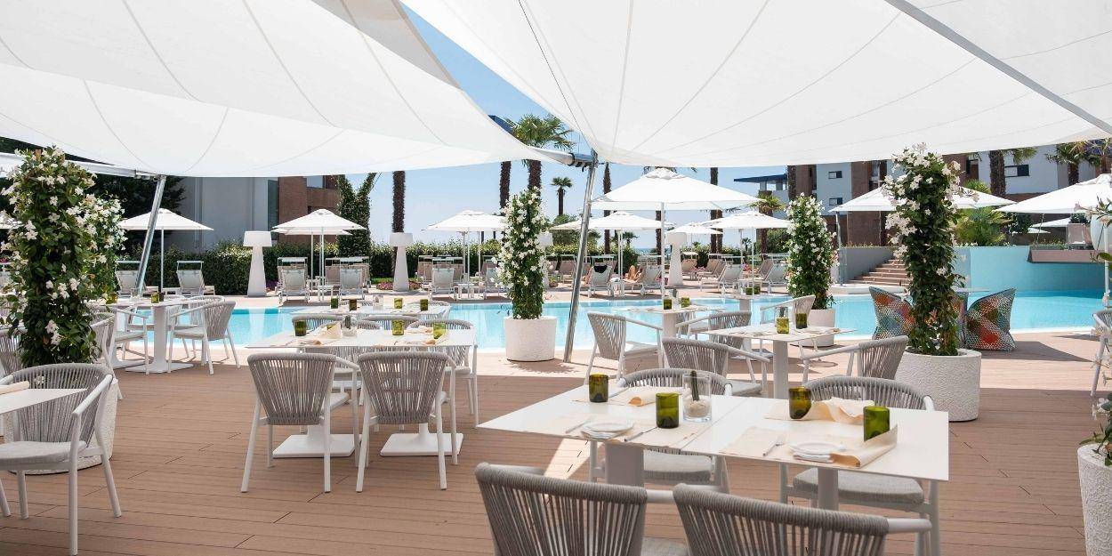 Outdoor pool lined with white loungers, trees and an al fresco dining terrace