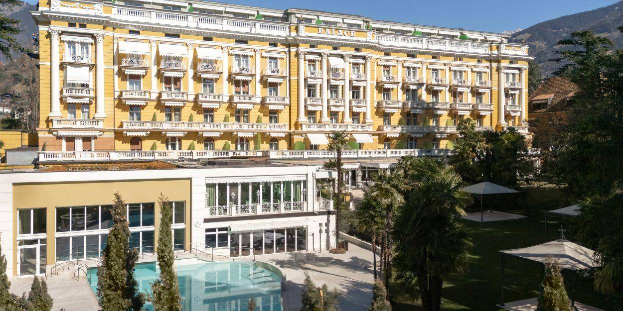 Landscaped gardens, a swimming pool surrounded by palms, and the exterior of Palace Merano