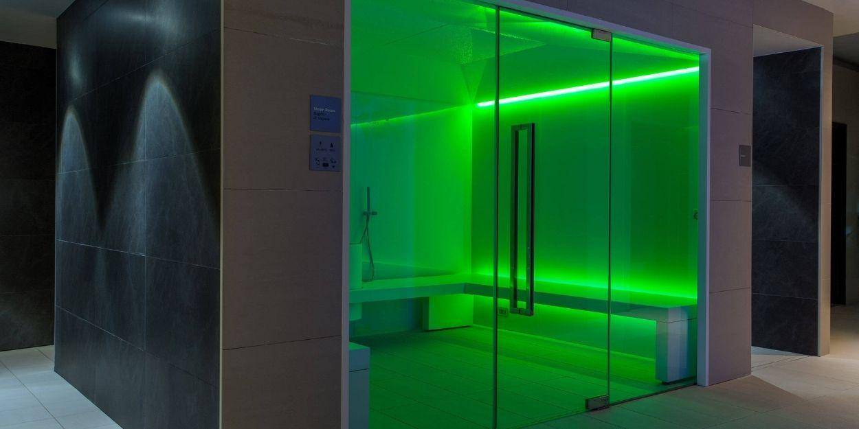 Green-lit steam room with a glass door 