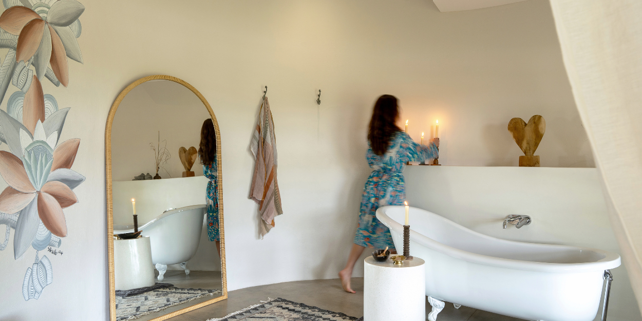 Luxe rustic bathroom with white walls, a freestanding bath, wooden sculptures, an arched mirror and floral wall murals