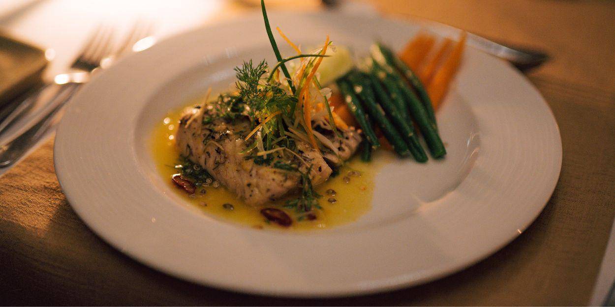 I dish of fish and fresh steamed vegetables in a yellow sauce 