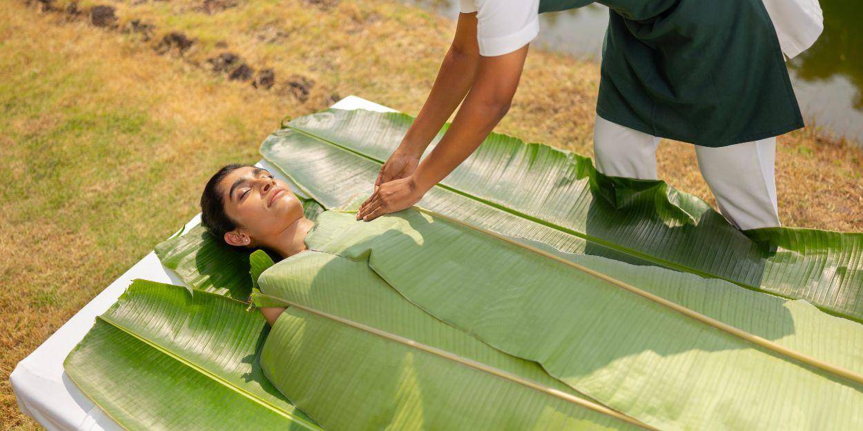 Female having an outdoor treatment done where therapist is wrapping her in banana leaves 