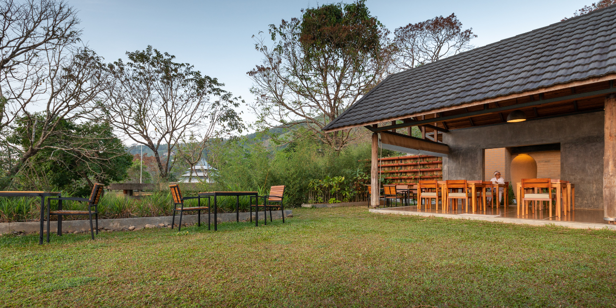 Traditional building with a tiled roof, stone walls and stilts, with an outdoor seating area and grassy lawn