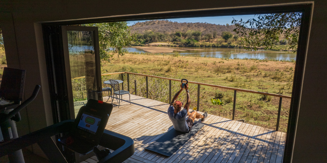 Man works out on a wooden deck with views of the African greenery and river