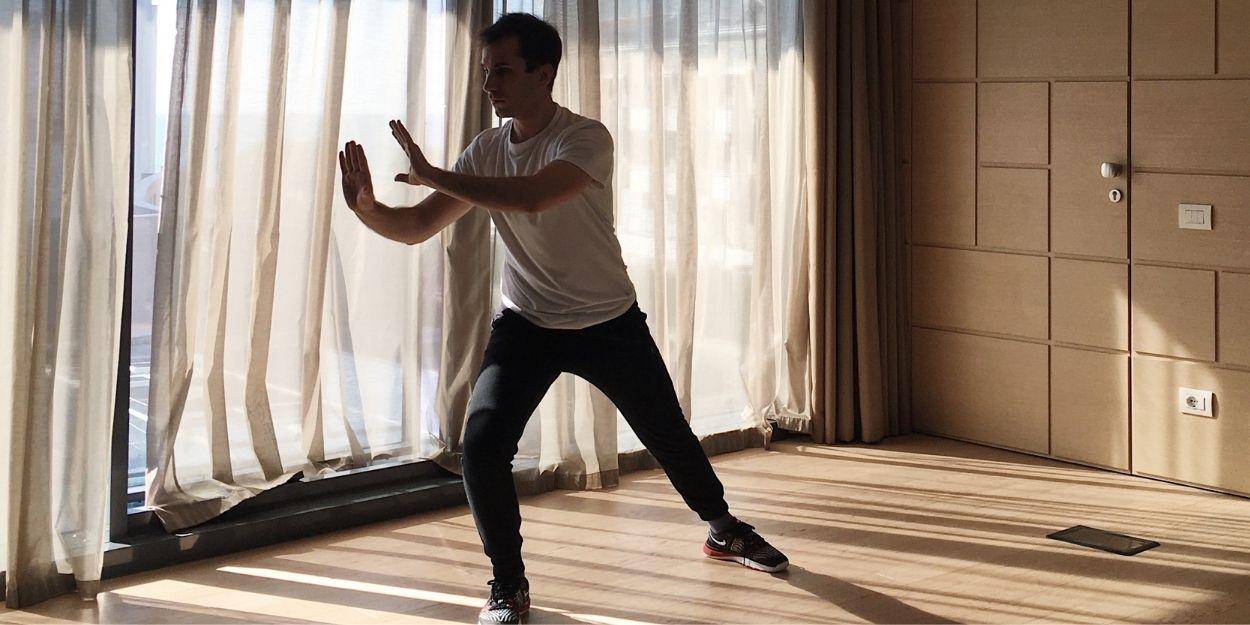 Man in a vest and tracksuit bottoms practices Tai Chi in an airy studio