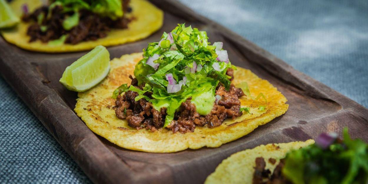 Nutritious cuisine at Palmaïa – The House of AïA Tacos topped with fresh salad and a lime garnish, laid out on a dark-wood tray