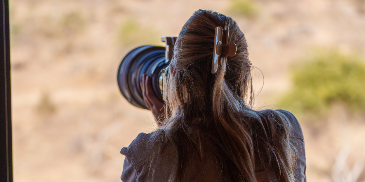 Woman with long hair in a clip takes pictures with a large professional camera in the African wilderness