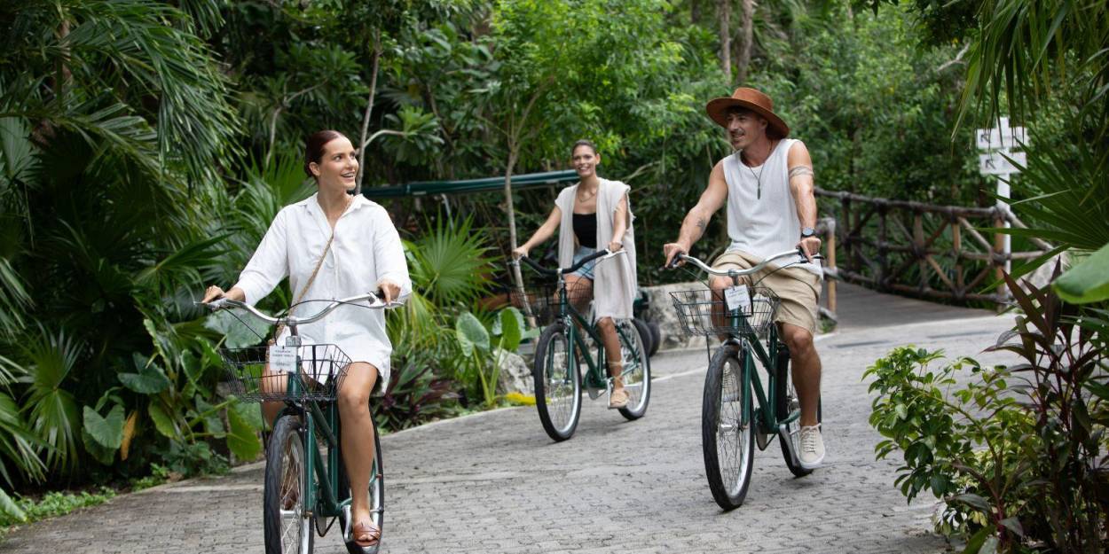 Cycling at Palmaïa – The House of AïA Two women and a man riding bikes on a path surrounded by tropical greenery