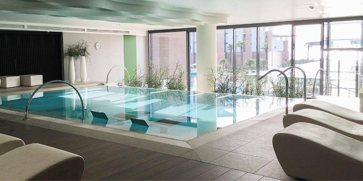 Sleek indoor pool surrounded by cubist crea, loungers and floor-to-ceiling windows