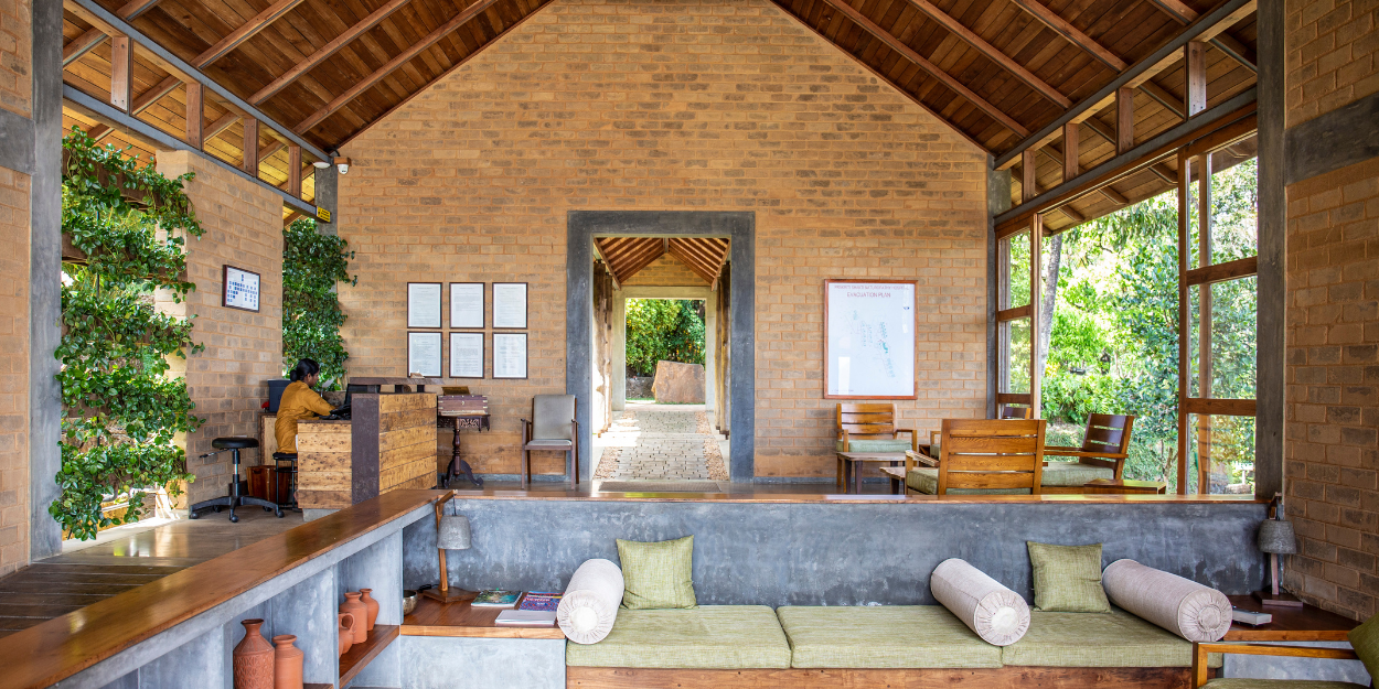 Cosy sofa area with neutral cushions in an airy room with a high wood-beamed ceiling, stone walls and foliage