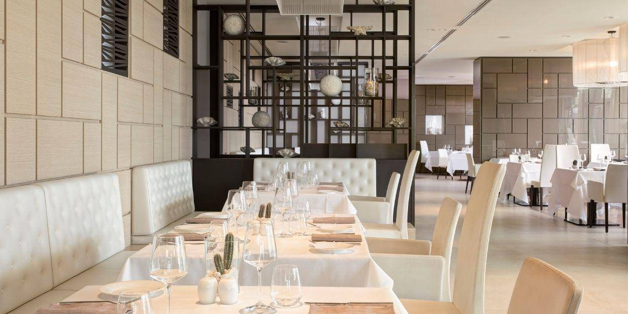 Airy restaurant with glossy tiled walls, dark-wood shelves stacked with ornaments, and white tablecloths