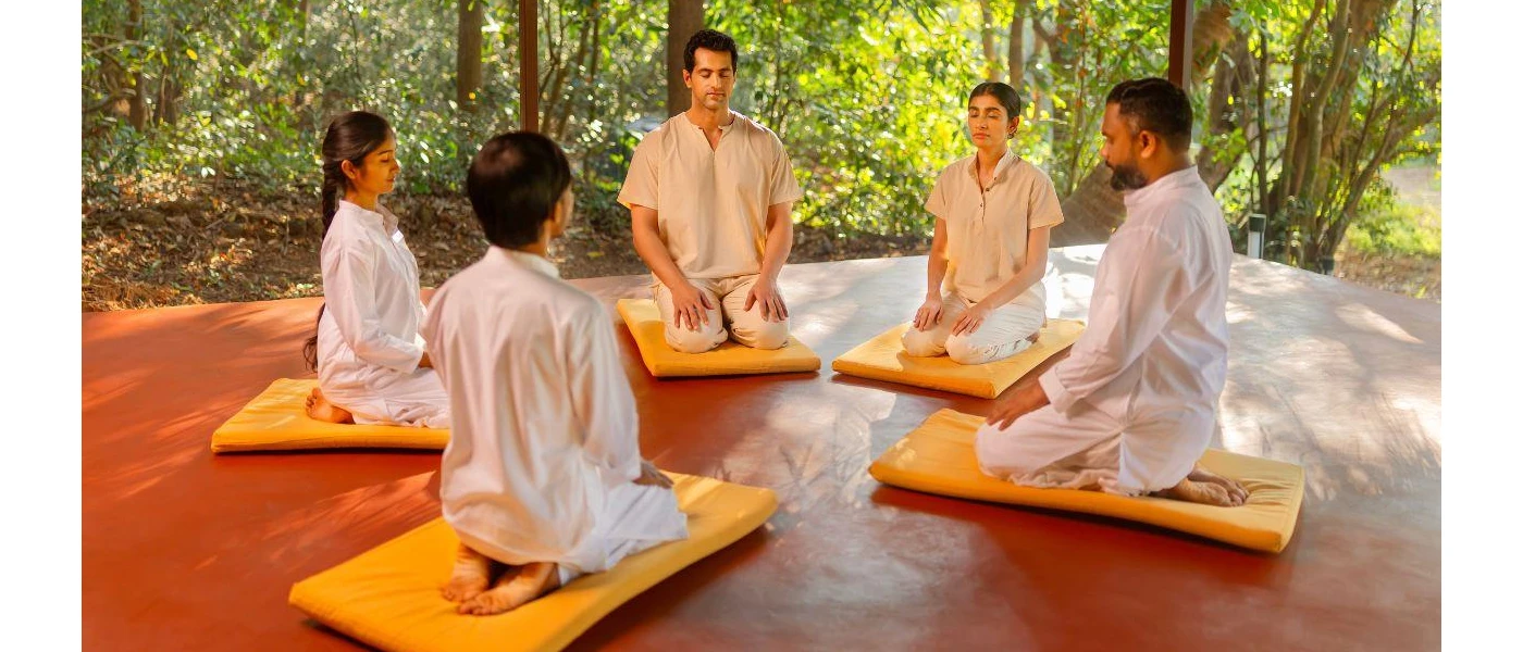 A group meditation in the open shala where guest sit on yellow cushions with their eyes closed 