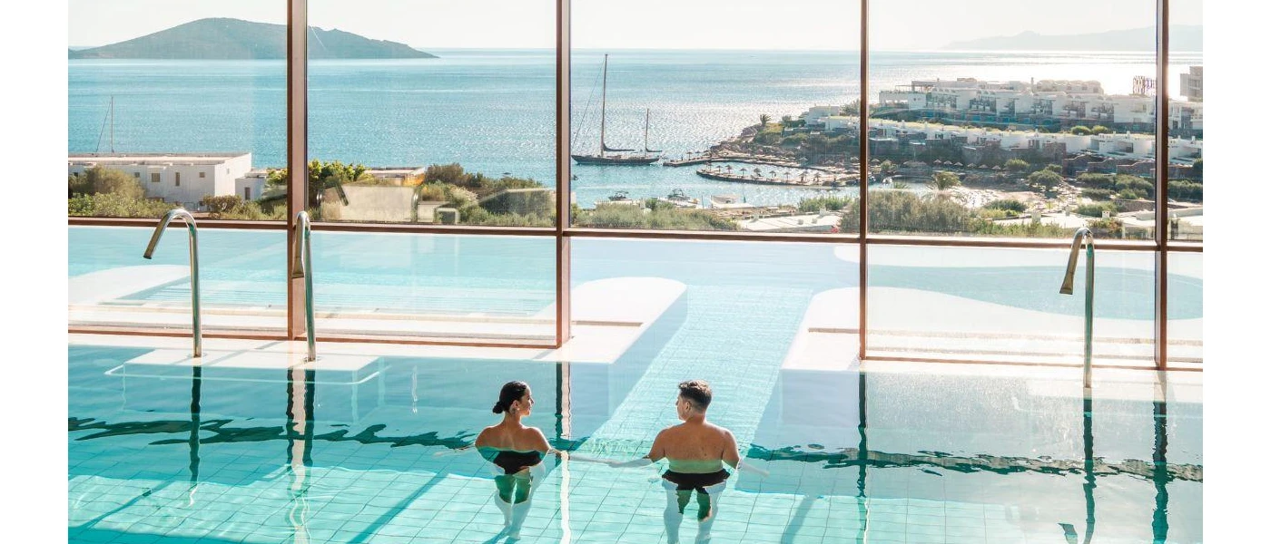 Couple relax in an indoor pool which leads outdoors and has views over the sea and islands
