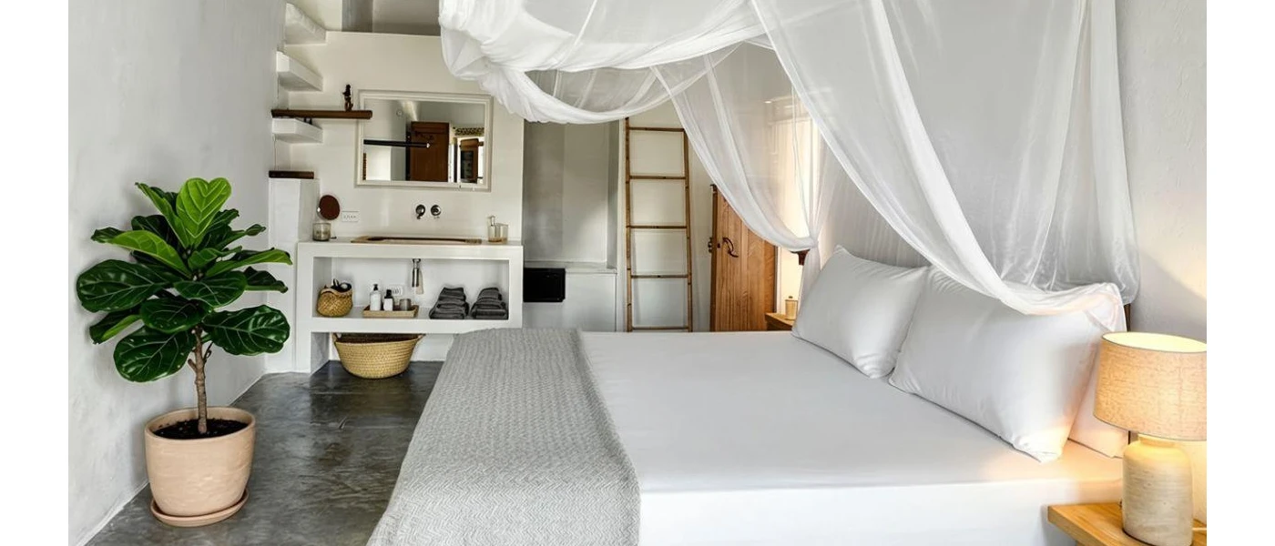 Bohemian-style bedroom with white bedding and a sheer white canopy, a potted plant and grey flooring