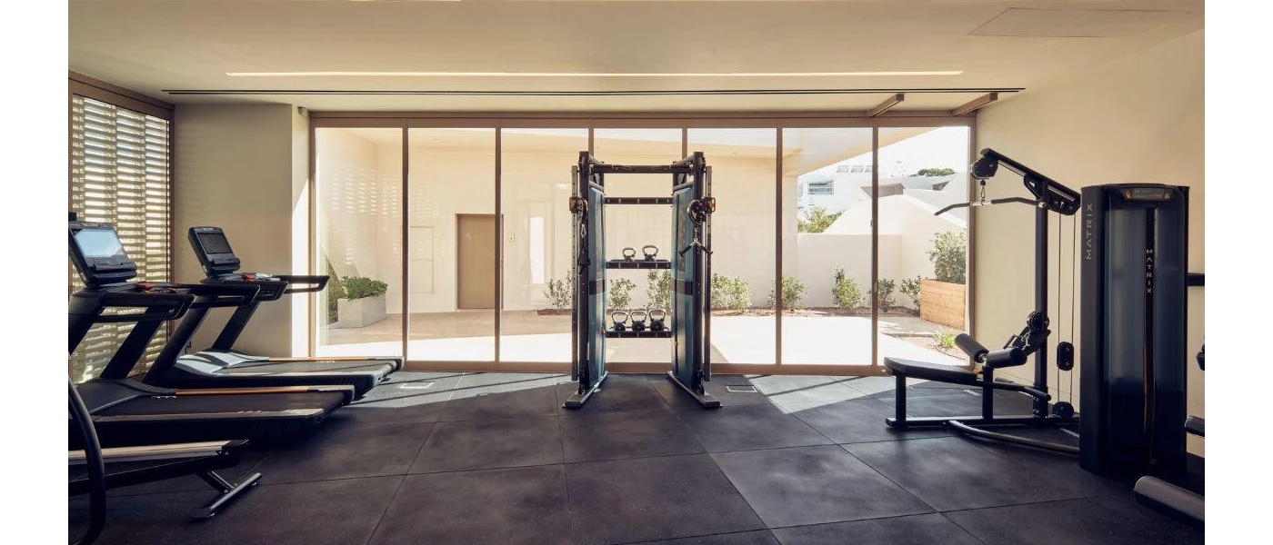 Gym with grey flooring and floor-to-ceiling windows overlooking a courtyard, with treadmills, weights machines and a bench