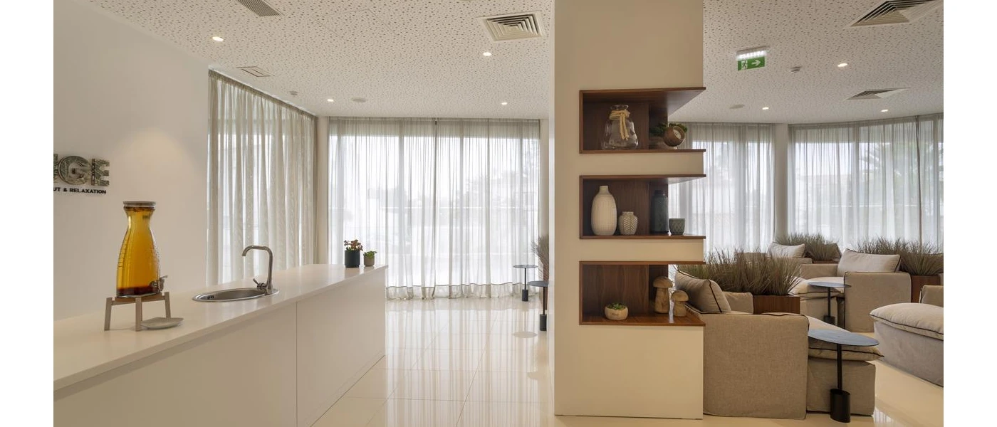 Modern room with full-length windows and sheer white curtains, cream sofas and a wooden chest with decorative vases