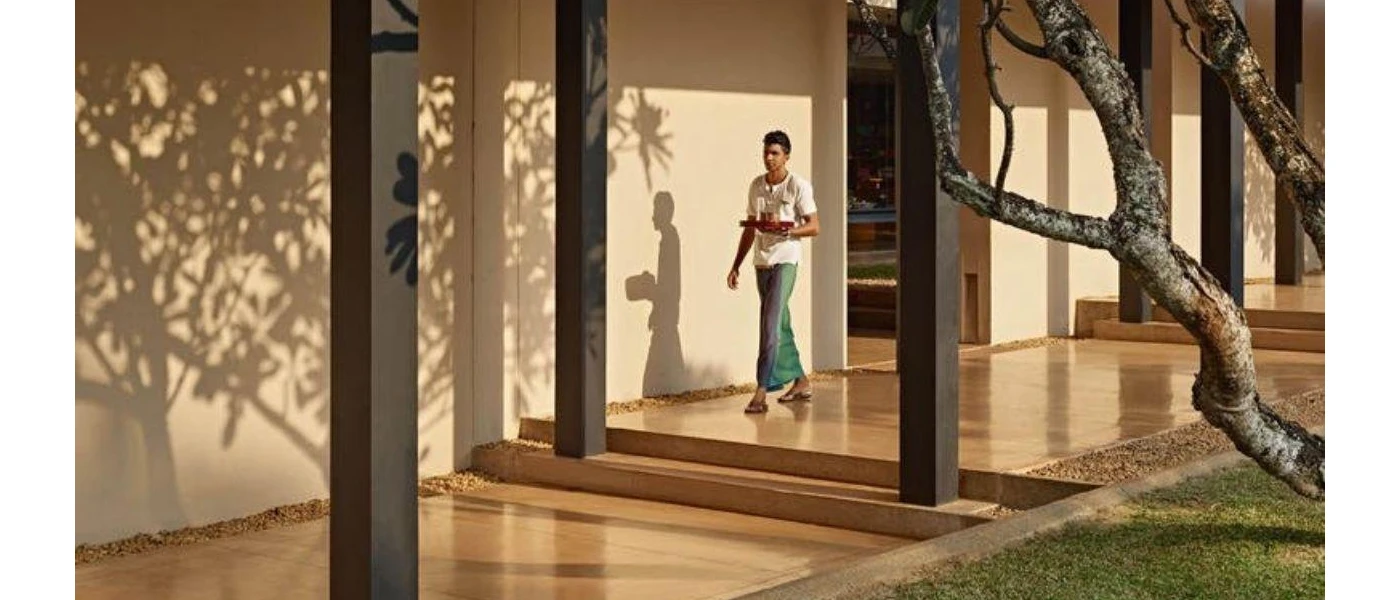 Staff member in traditional Sri Lankan dress walking through an open-air corridor with a tray of tea