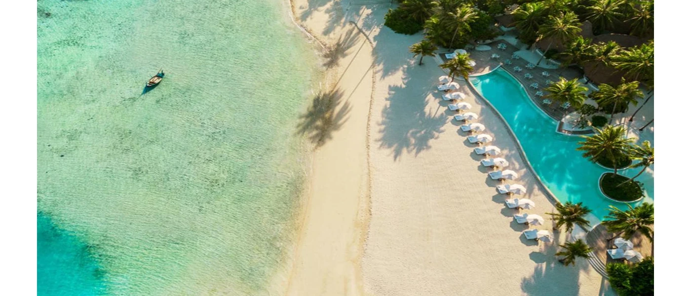 White sandy beach, swimming pool and line of sunbeds overlooking clear turquoise shallows