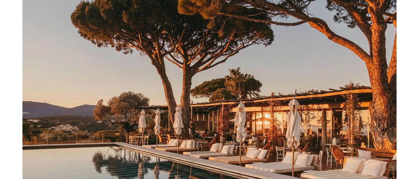 Swimming pool fringed with trees and views of the distant hills, surrounded by chic striped daybeds and white umbrellas