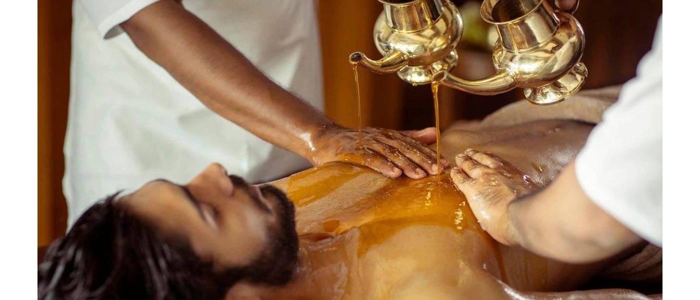 Man lies on his back as oil is poured onto his chest and two therapists guide the stream
